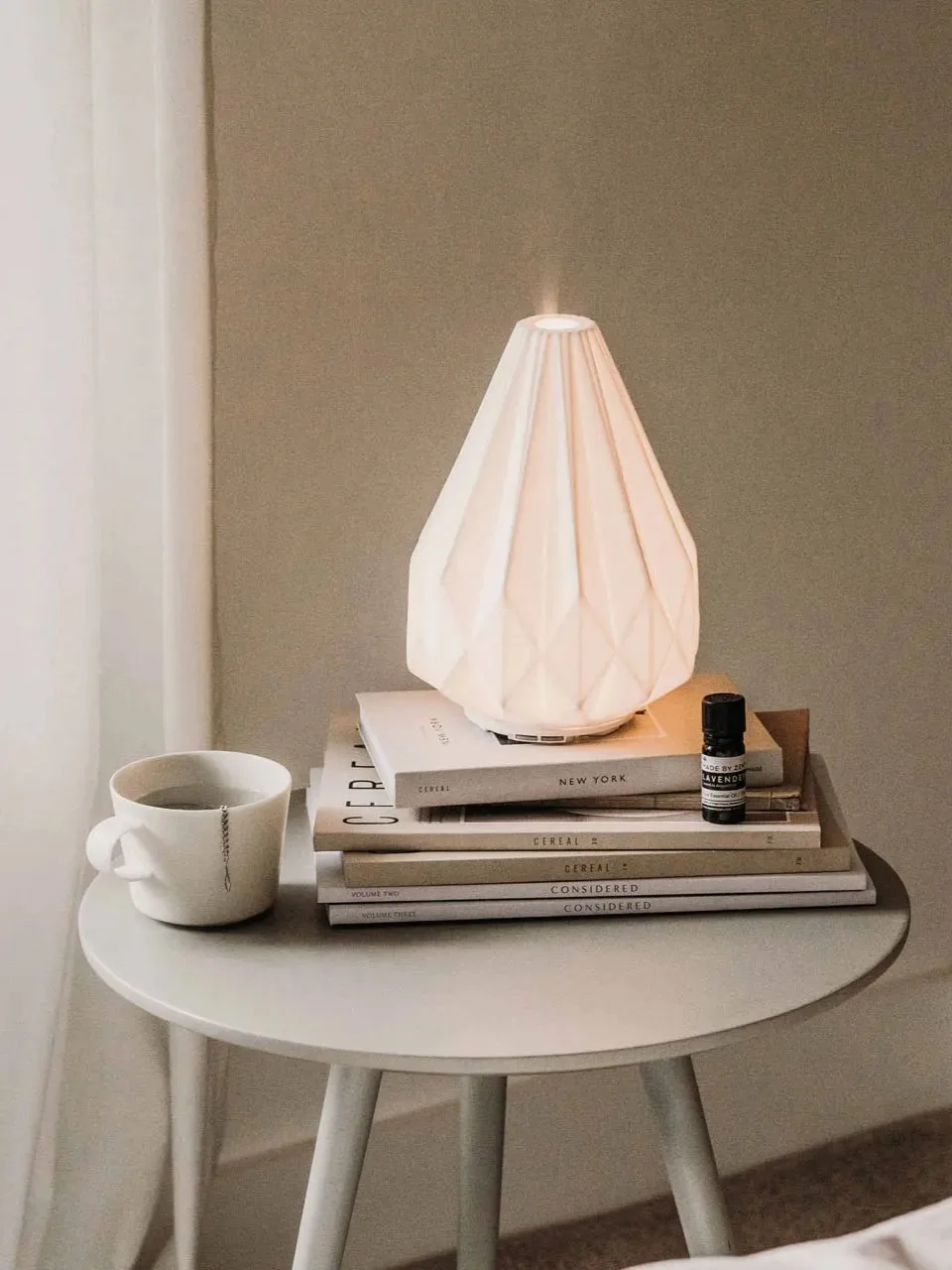 Ceramiczny dyfuzor na stosie książek i filiżanka z herbatą na minimalistycznym stoliku